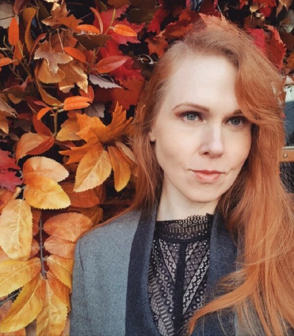 Portrait image of woman with red hair and autumn foliage in background.